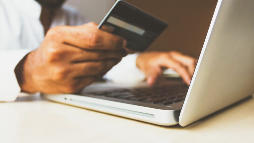 A hand holding a credit card in front of a laptop during an online payment